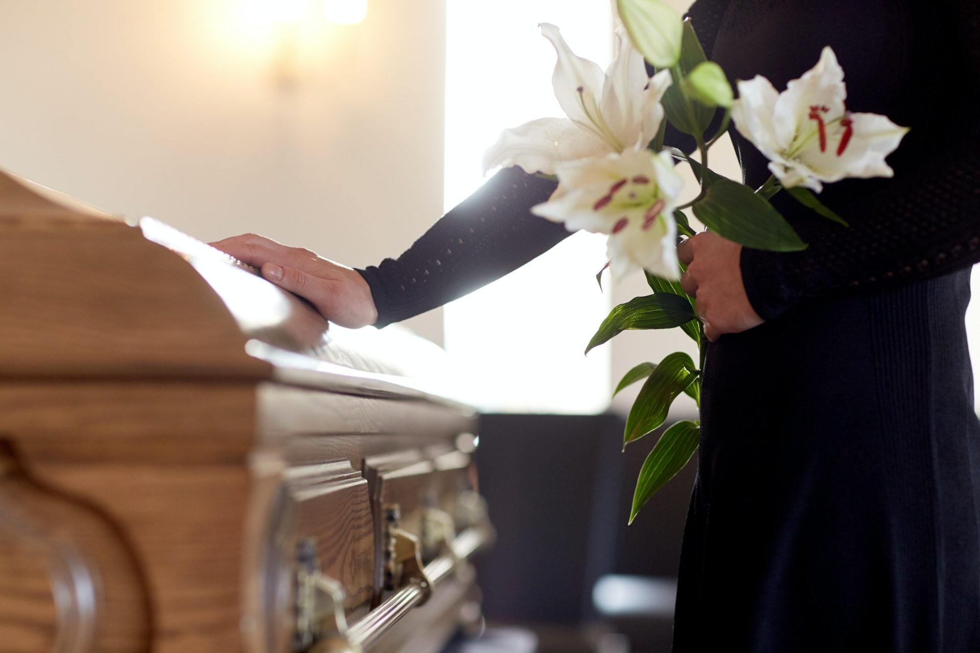 woman-with-lily-flowers-and-coffin-at-funeral-e1636906897650